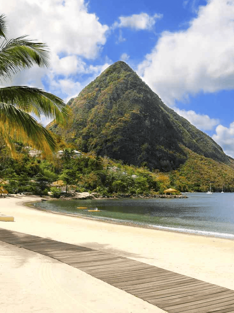 Lush tropical island with mountain, sandy beach, and palm trees in clear blue ocean water.