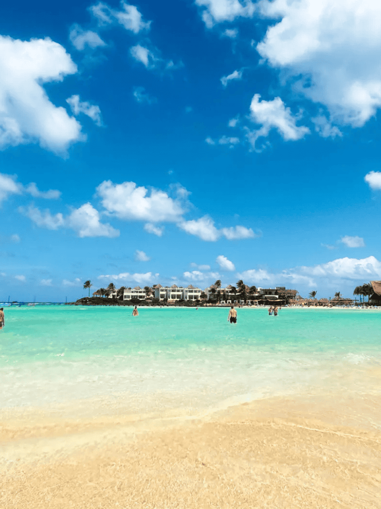 Bright blue sky with fluffy clouds over clear turquoise ocean and sandy beach, perfect for travel and vacation.