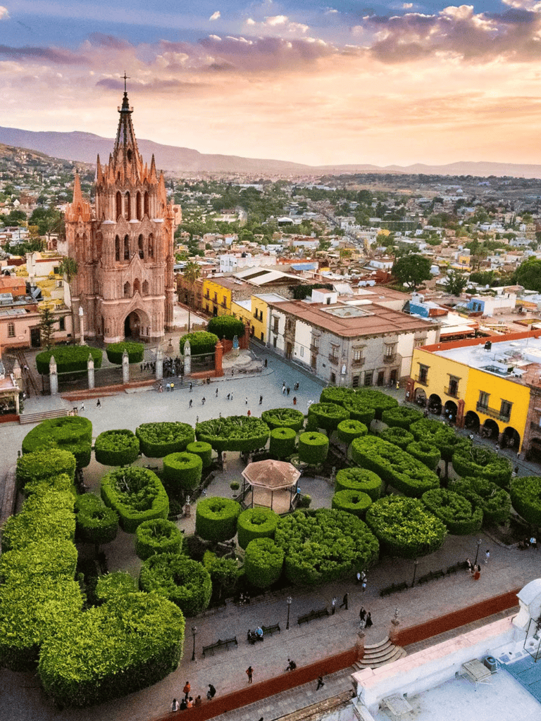 Colorful historic town square with a Gothic church and manicured green gardens at sunset.