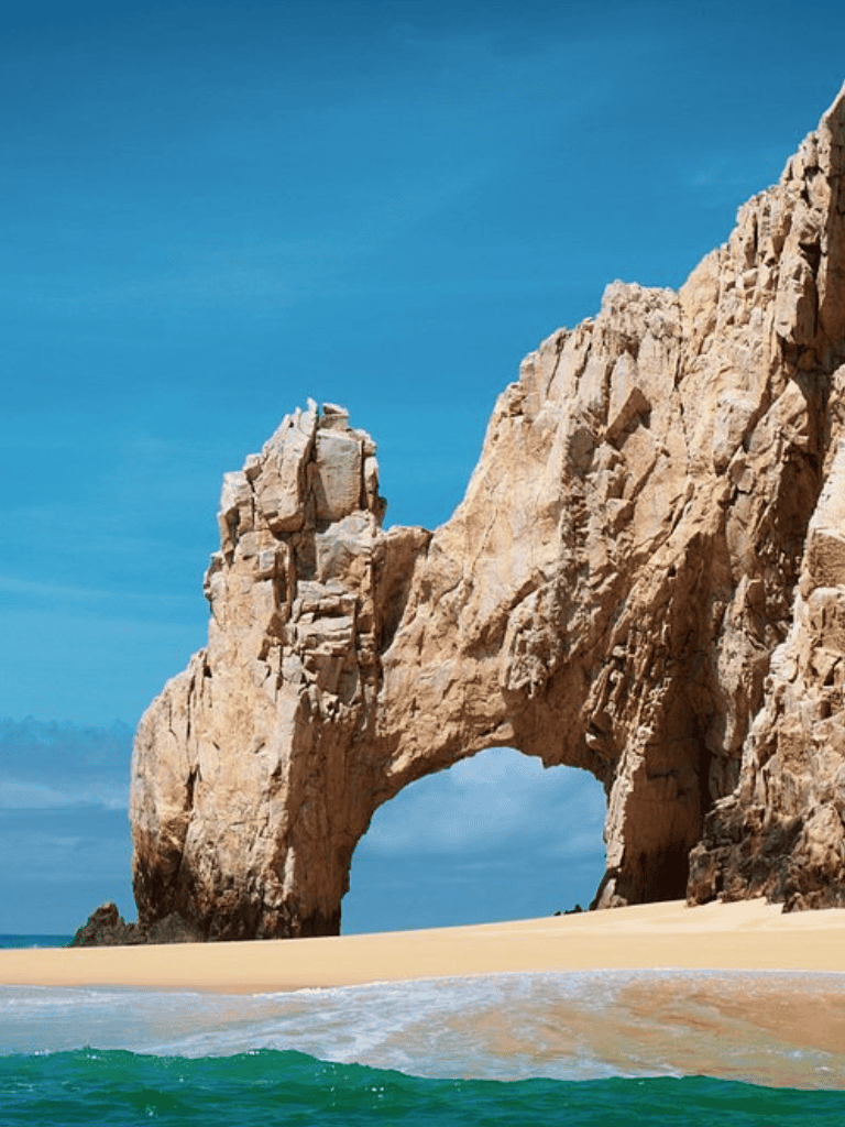 Vivid coastal rock formation with natural arch under bright blue sky, ocean waves crashing at the beach.