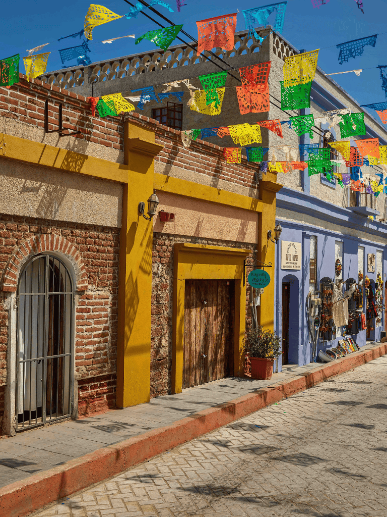 Colorful papel picado decorations hanging above vibrant street scene in Mexico.