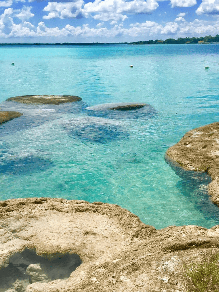 Calm turquoise water with rocks along shoreline, scenic ocean view.