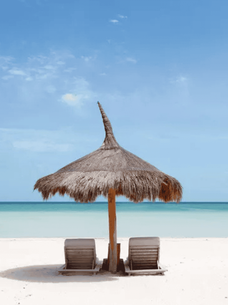 Relaxing beach scene with straw umbrella and lounge chairs by the ocean, perfect for vacation planning.