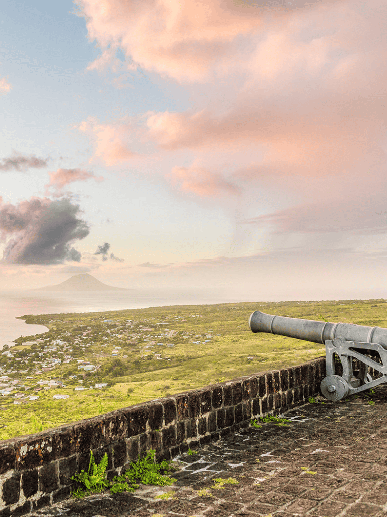 Breathtaking coastal view with historical cannon overlooking a scenic landscape at sunset.