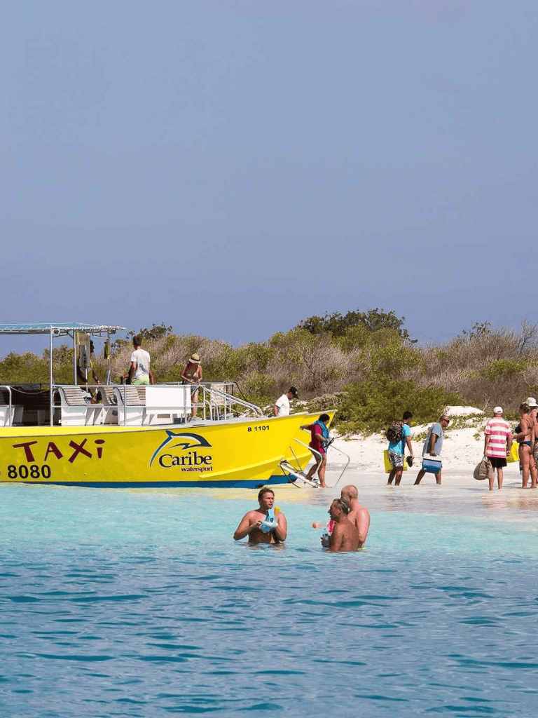 Relaxing beach scene with a yellow Caribbean water taxi, tourists swimming, and shoreline activities at Quest for Directions.