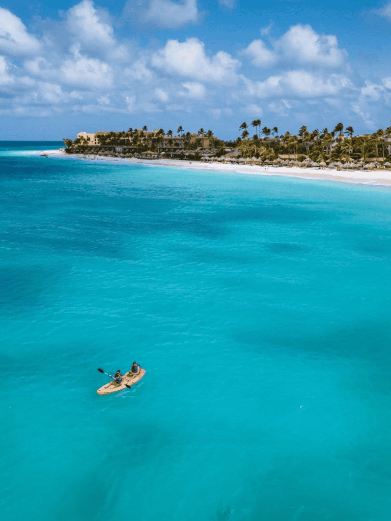 Bright turquoise ocean with a kayaker near a tropical beach resort with palm trees and white sand.