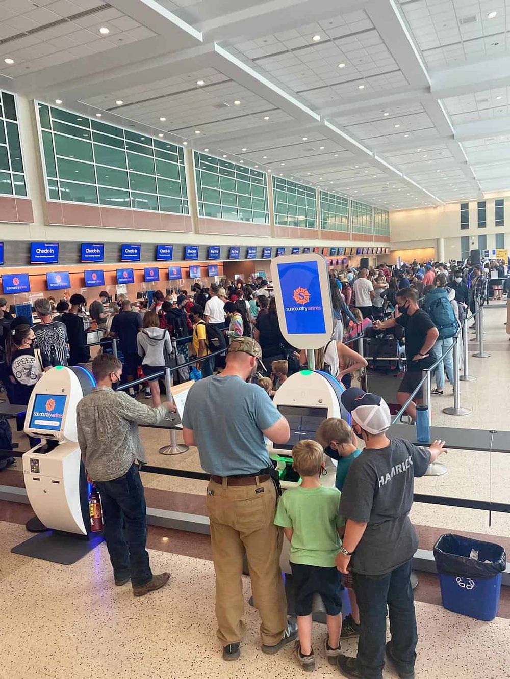 Crowded airport check-in area for Sunny Ways airlines, passengers waiting in line with luggage.