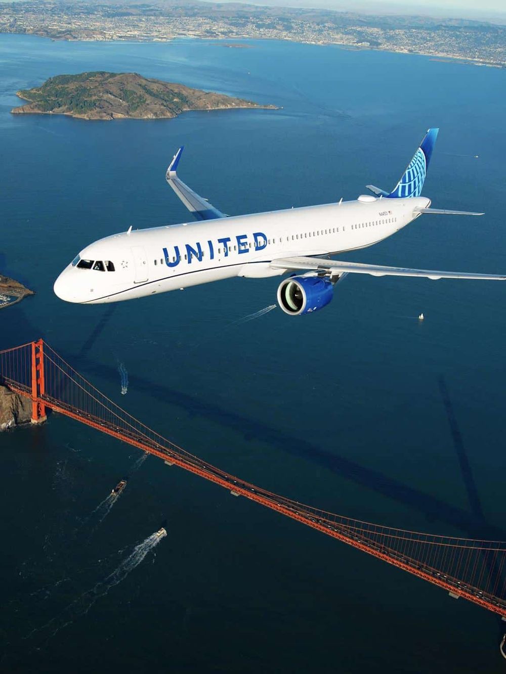 Commercial airplane flying over the Golden Gate Bridge with San Francisco bay in background.