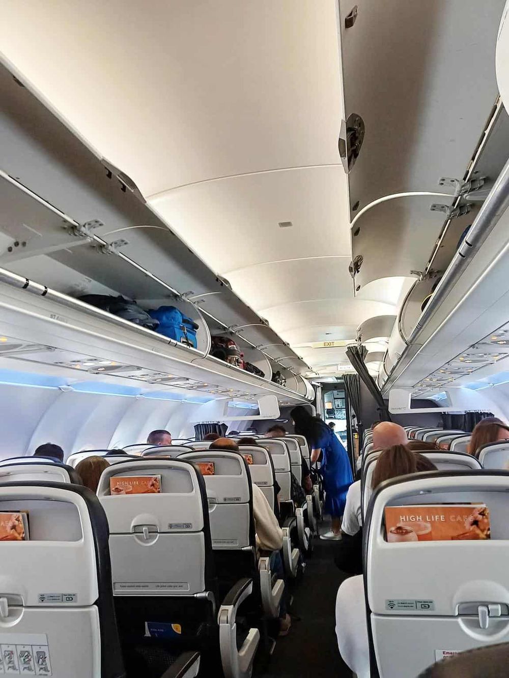 Comfortable airplane interior with passengers seated, overhead storage, and flight attendant assisting.