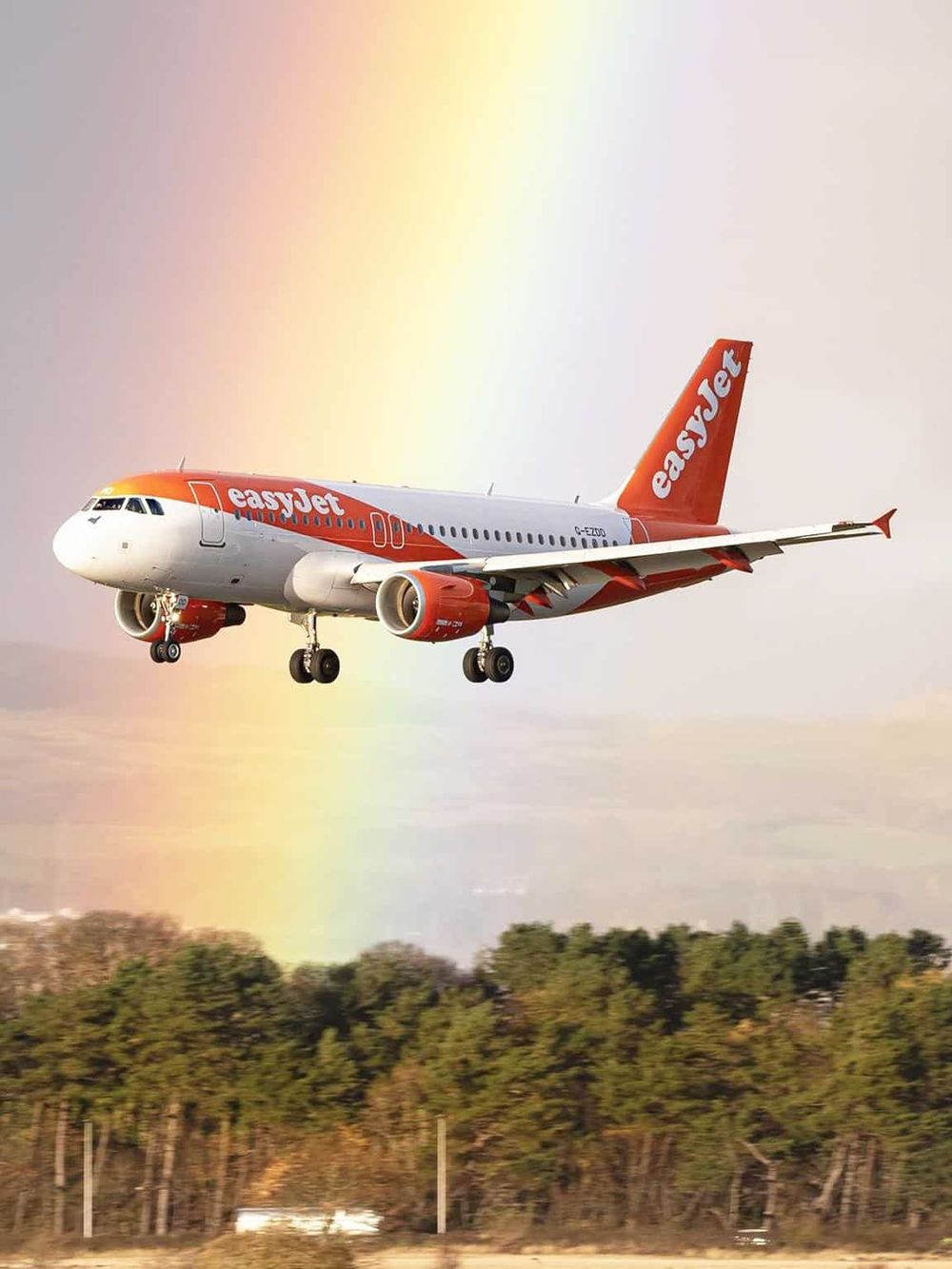 EasyJet airplane flying in the sky with a rainbow background.