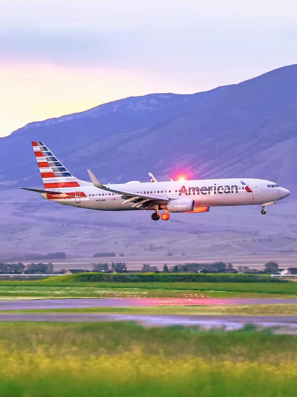 American Airlines airplane taking off from runway at sunset, scenic mountain background.