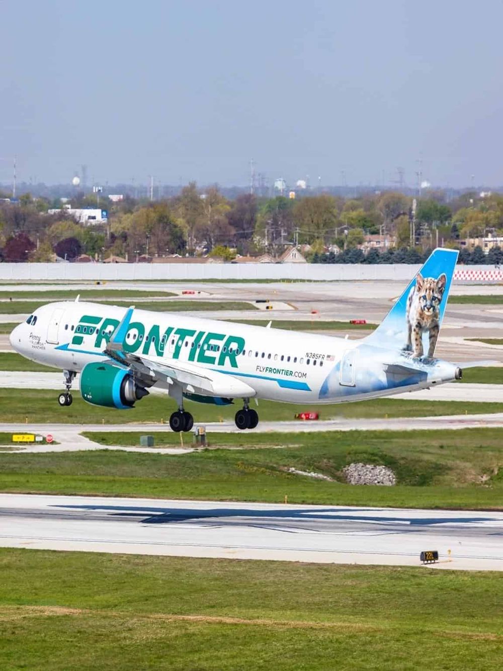 Airplane with Frontier Airlines branding, tiger decal on tail, ground taxiing at airport.