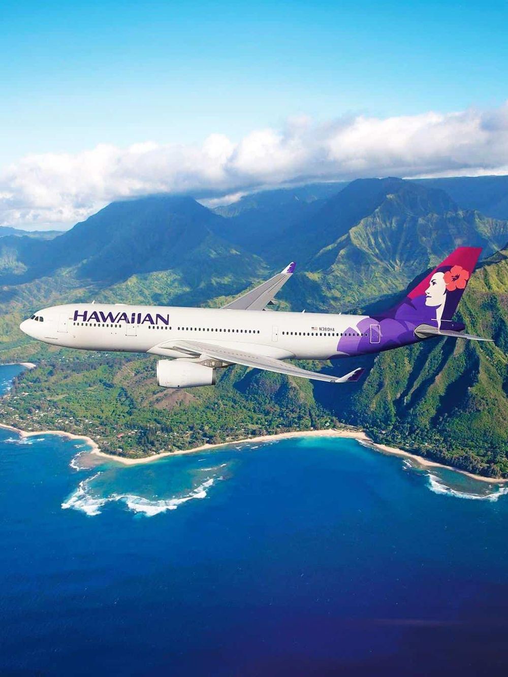 Hawaiian Airlines airplane flying over lush Hawaiian coastline and volcanic mountains.