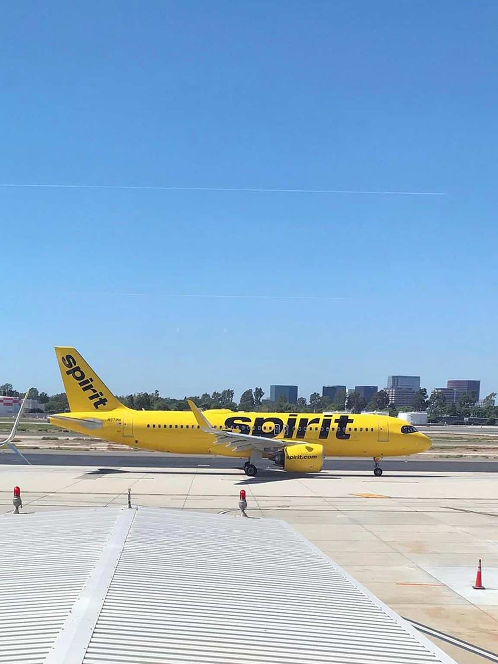 Spirit Airlines aircraft on runway at airport with city skyline in background.