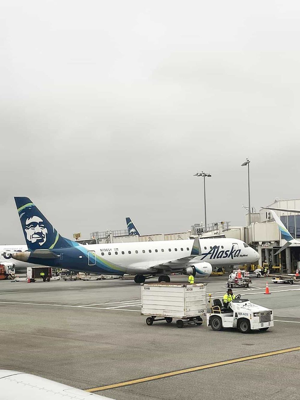 Alaska Airlines airplane at airport gate with ground crew and luggage cart in view.