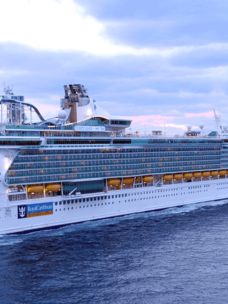 Luxury cruise ship sailing on the ocean, Royal Caribbean branded vessel, scenic sunset background.