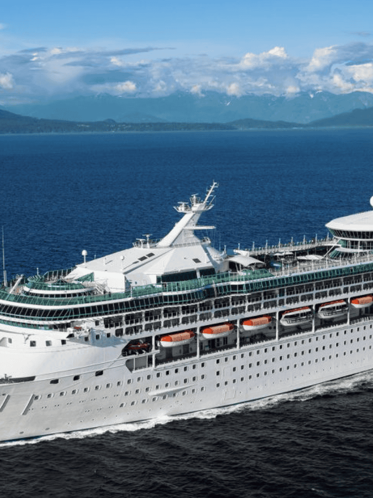 Luxury cruise ship sailing in open ocean with scenic mountains background.