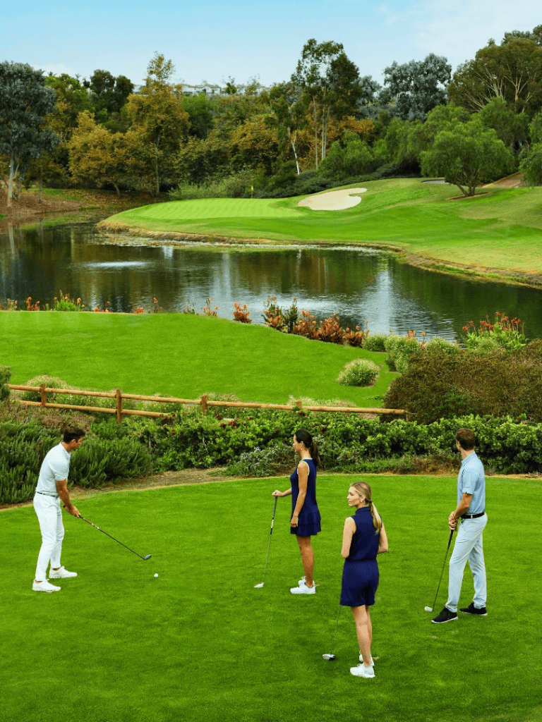 Luxurious golf course with water hazard and four golfers practicing their swings. Perfect for golf enthusiasts and outdoor recreation.