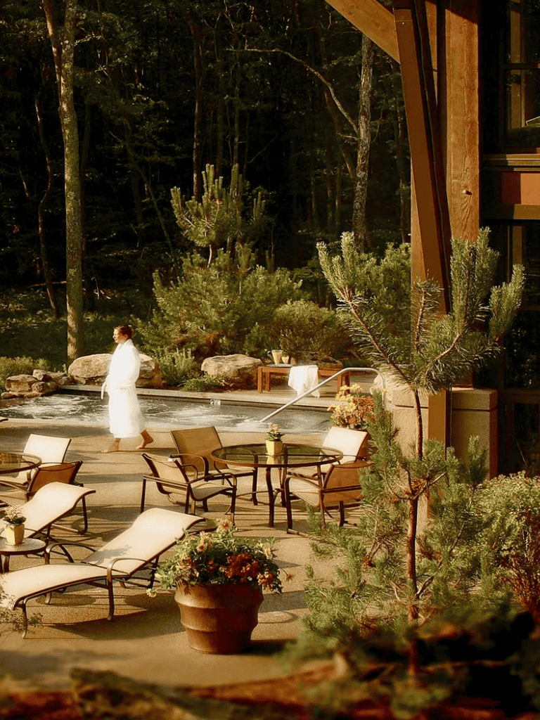 Relaxing outdoor hot tub in forest setting with lounge chairs and wood cabin, perfect for nature retreat.