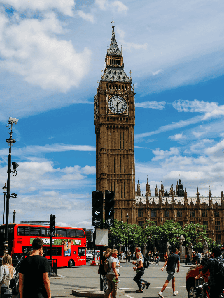 Historic Big Ben clock tower in London cityscape, busy street with pedestrians and red double-decker bus.