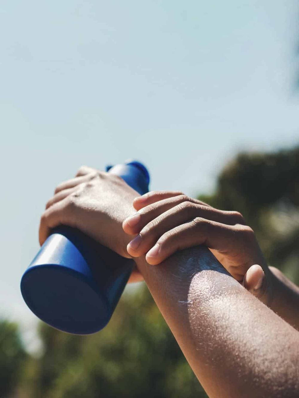 Bright outdoor shot of a person gripping a blue water bottle with hands, symbolizing adventure and hydration.