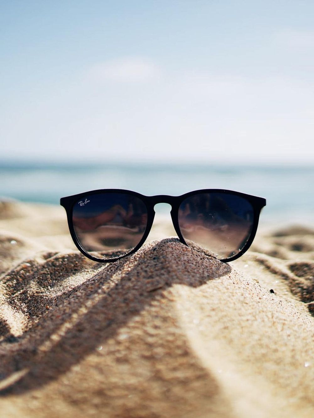 Sunglasses on sandy beach with ocean background, travel accessories for beach vacation.