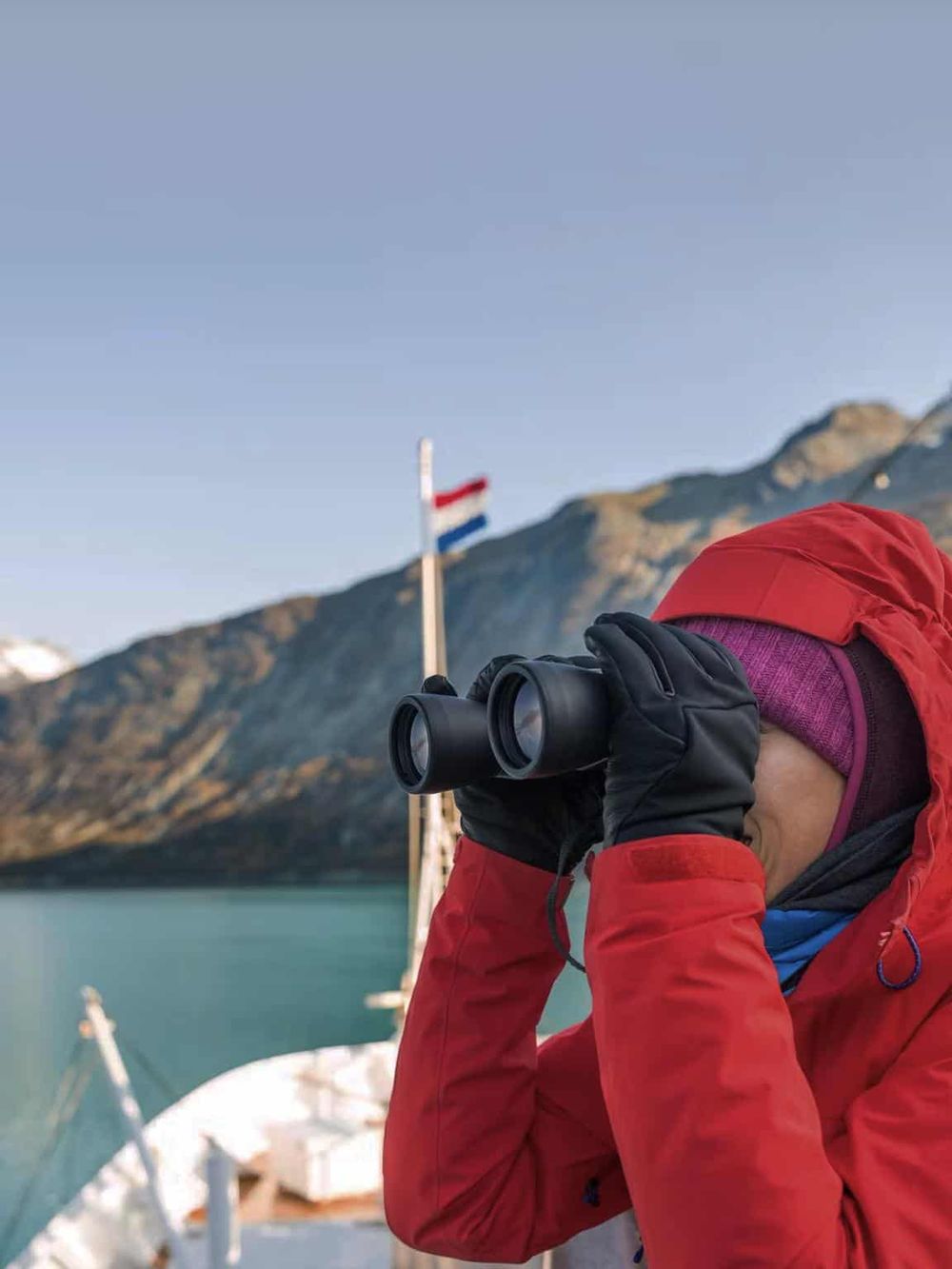 Stunning mountain landscape with a person in red jacket using binoculars near a boat.