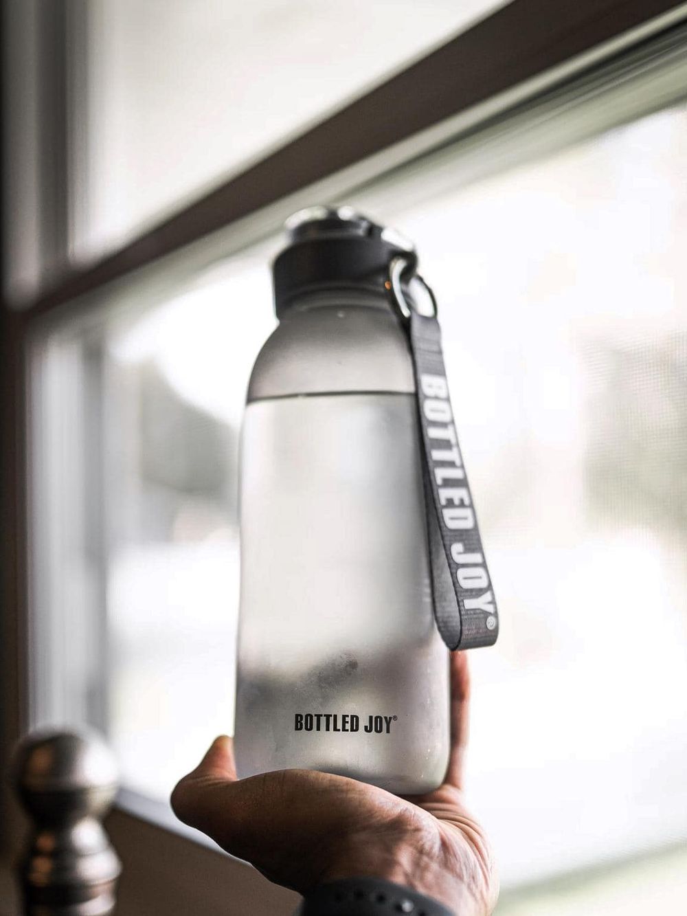 Sustainable water bottle with BOTTLLED JOY strap, eco-friendly hydration for active lifestyles.