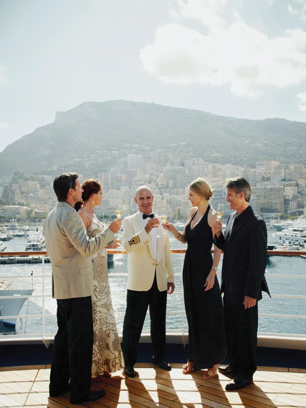 Elegant yacht crew celebrating with guests on deck, stunning harbor view, luxury maritime experience.