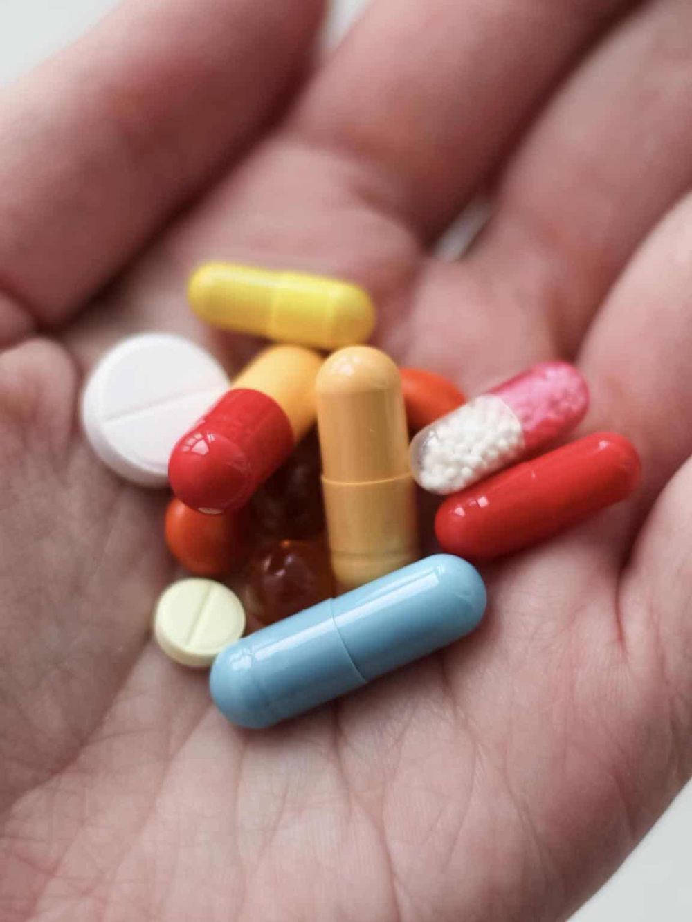Assorted prescription pills and capsules in a person's hand for medication management.