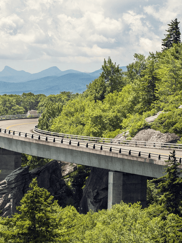 Serene mountain highway passing through lush green forest with distant mountain range.