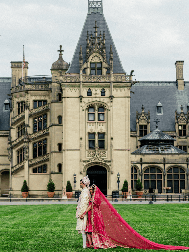 Elegant couple in traditional Indian wedding attire in front of a grand castle-like hotel.