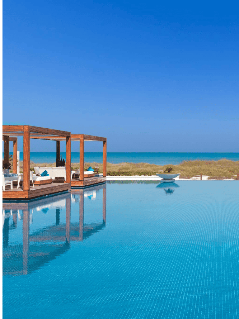 Luxurious swimming pool with ocean view and outdoor lounge area, perfect for beachside relaxation and vacation.