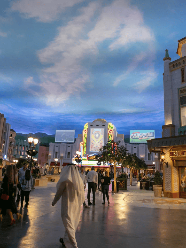 Vibrant theme park at dusk with illuminated rides and attractions, lively crowd, and colorful architecture in Las Vegas.