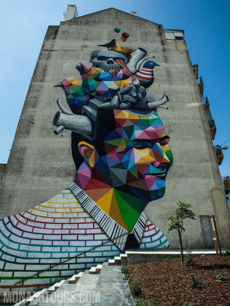 Vibrant geometric mural of a man's profile with surreal colorful elements on a city building wall.