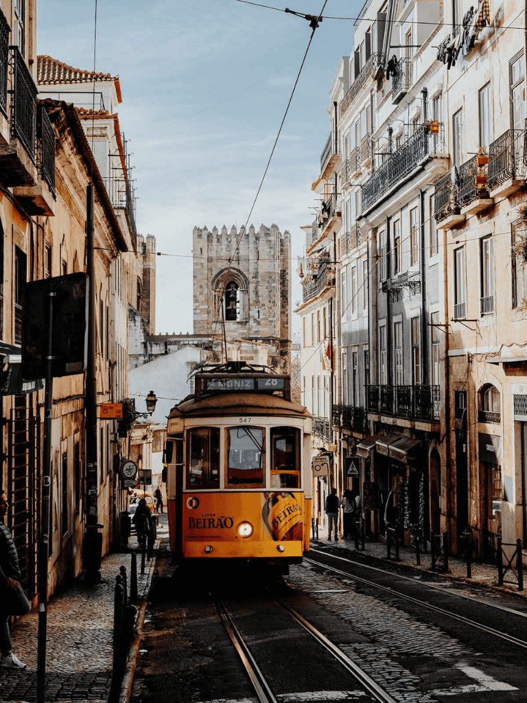 Vintage tram traveling historical streets of Lisbon, Portugal, near iconic cathedral.