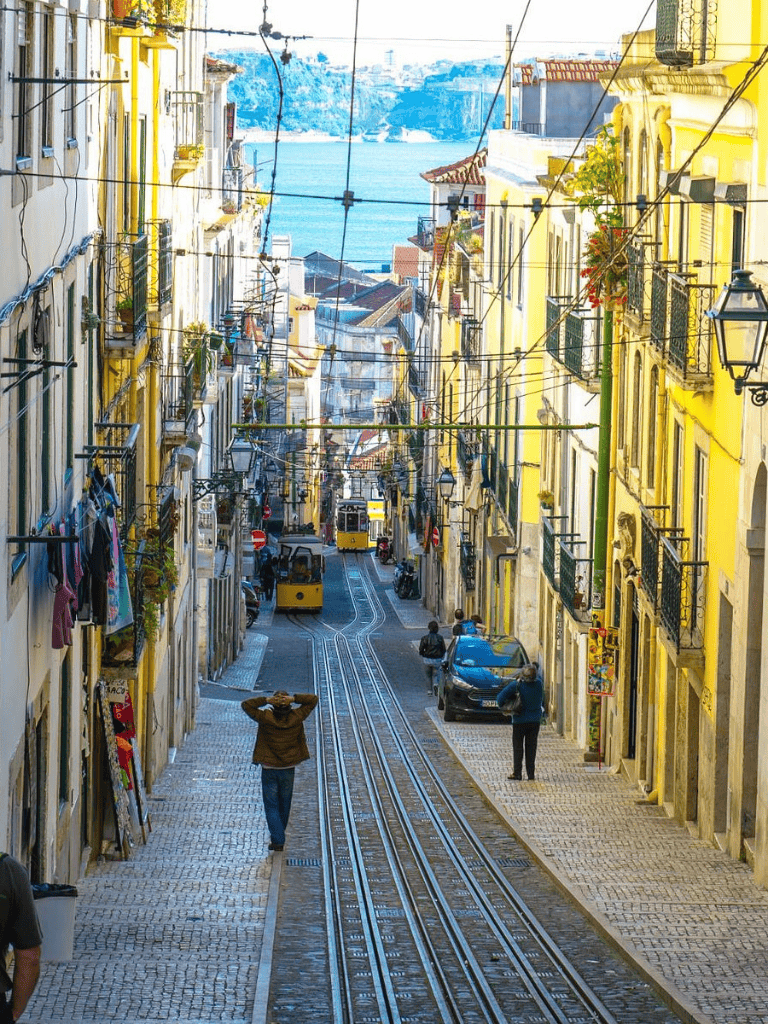 Smiling colorful Lisbon street with tram tracks, historic buildings, and scenic river view in Portugal.