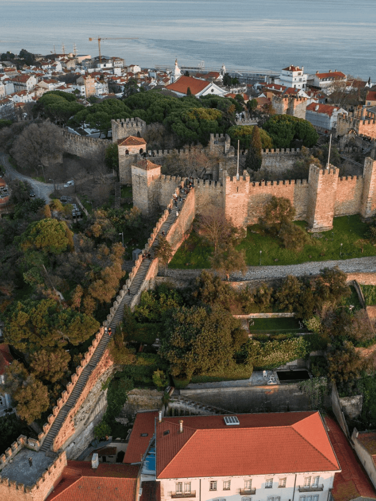 Medieval castle walls and scenic coastal town viewed from above, historical architecture and lush greenery.