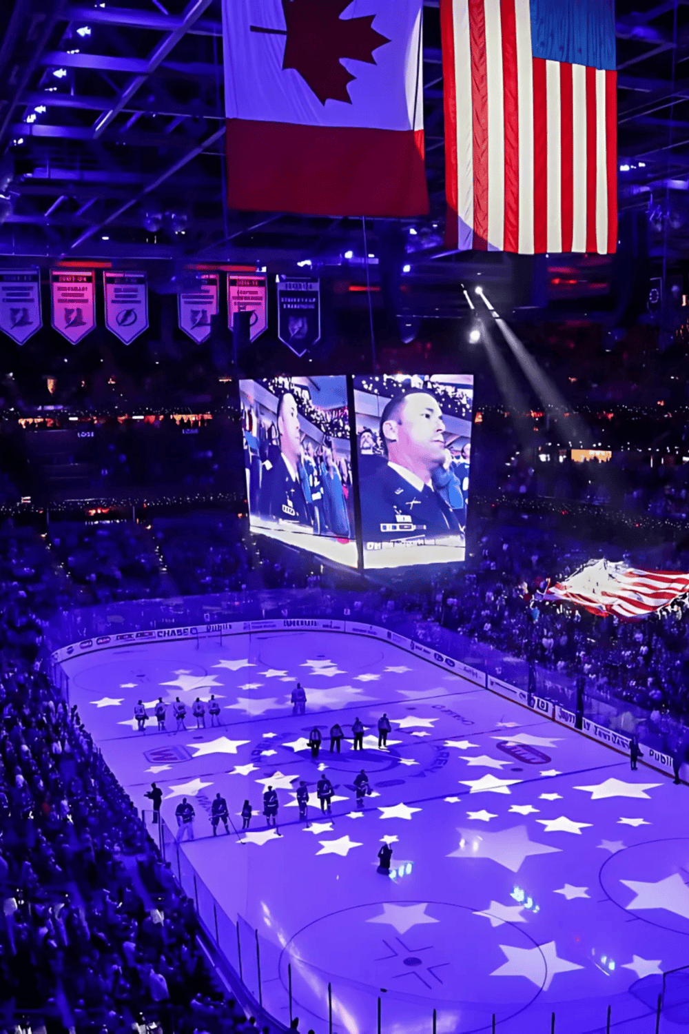 United States flag hanging at an NHL game with players on ice and large screens showing a player’s face.