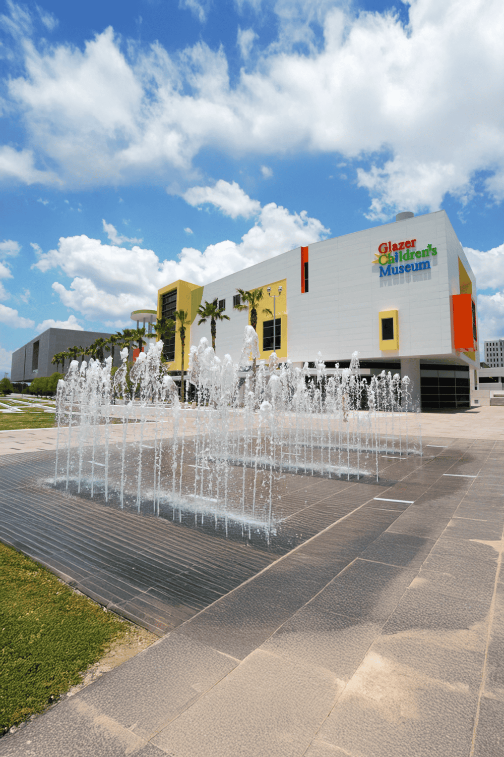 Colorful Glazer Children's Museum with outdoor fountain and palm trees under bright blue sky.