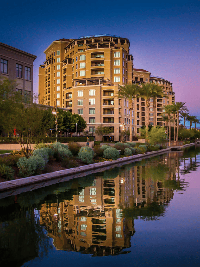 Luxury waterfront apartment building with palm trees during sunset.