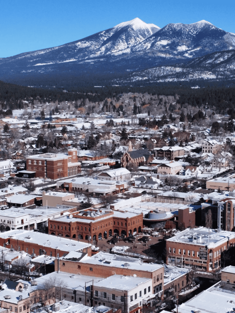 Historic downtown mountain town with snow-covered buildings and majestic snow-capped peaks in background.