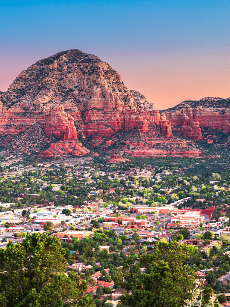 Vibrant cityscape of Sedona at sunset with iconic red rock formations and lush greenery.