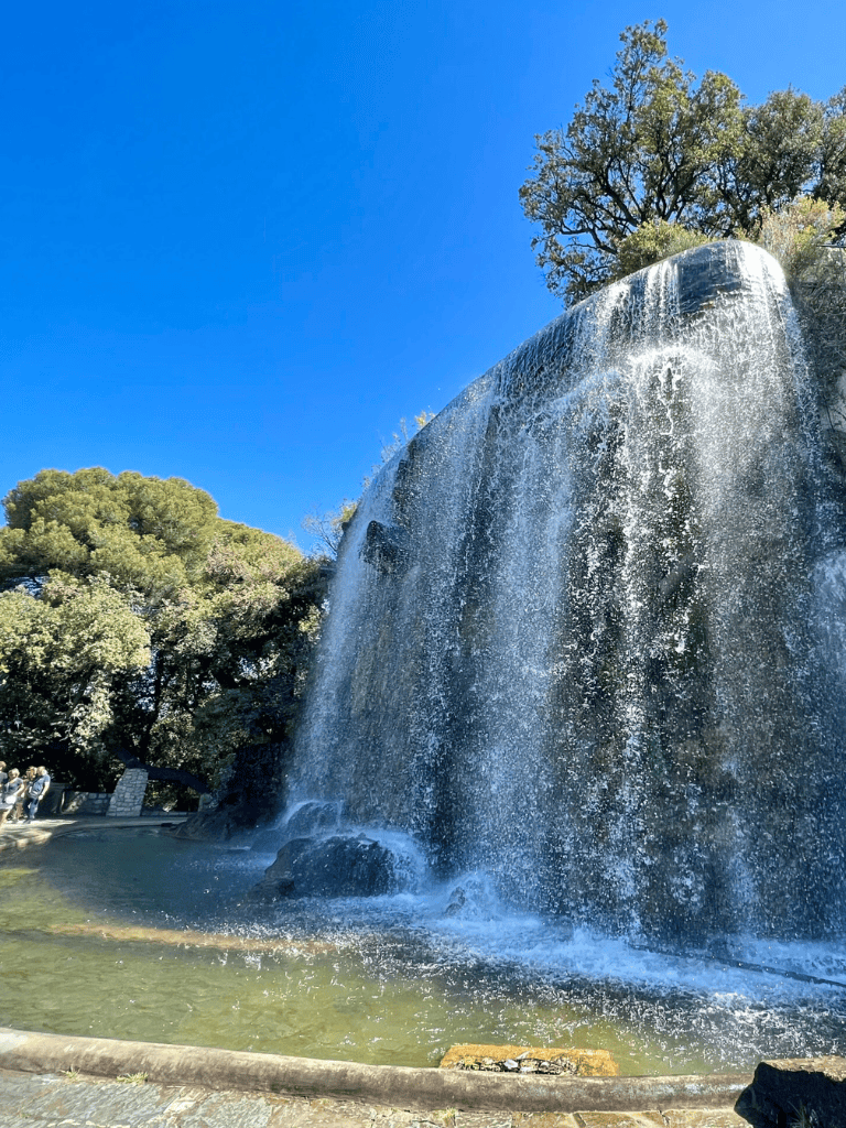 Vibrant waterfall at Quest for Directions park with lush green trees and clear blue sky.