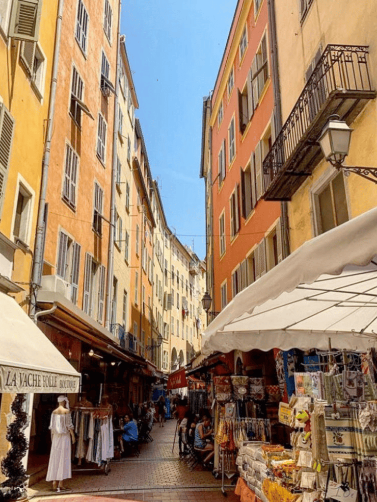 Colorful Mediterranean street scene with outdoor market stalls and vibrant building facades in Nice, France.