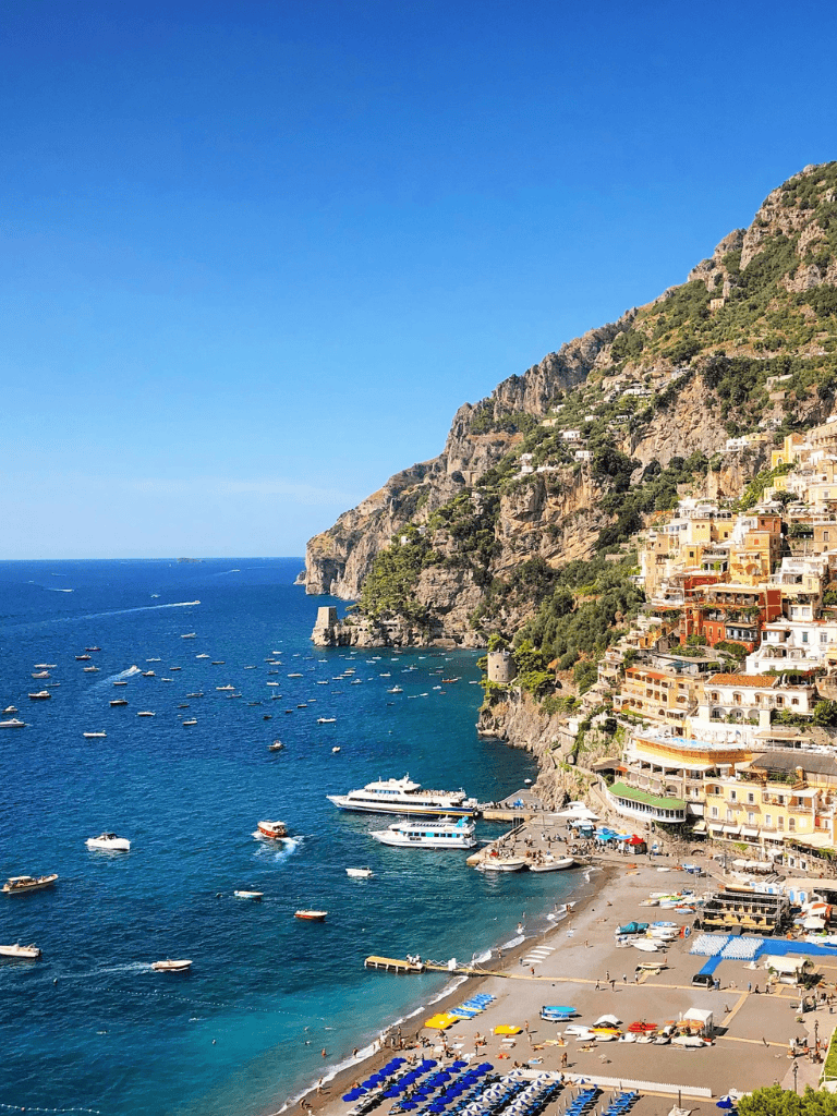 Vibrant coastal town with colorful houses and boats in the sea, scenic mountain backdrop, sunny day.