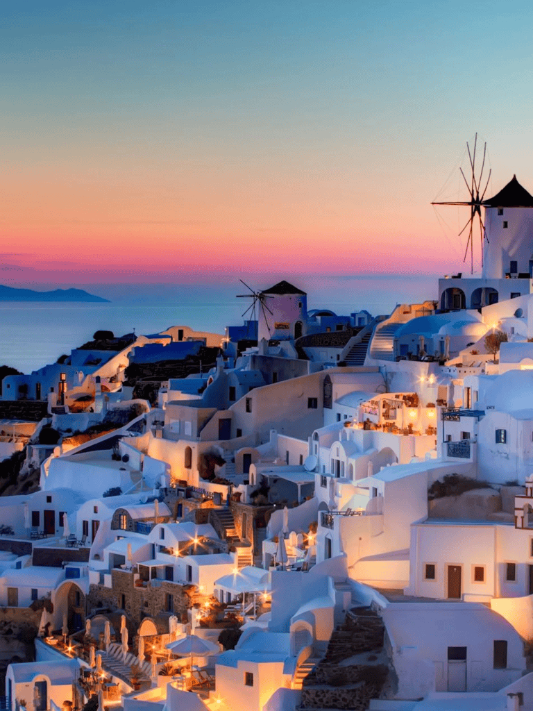Traditional Greek island village at sunset, whitewashed buildings, windmills, aerial view.