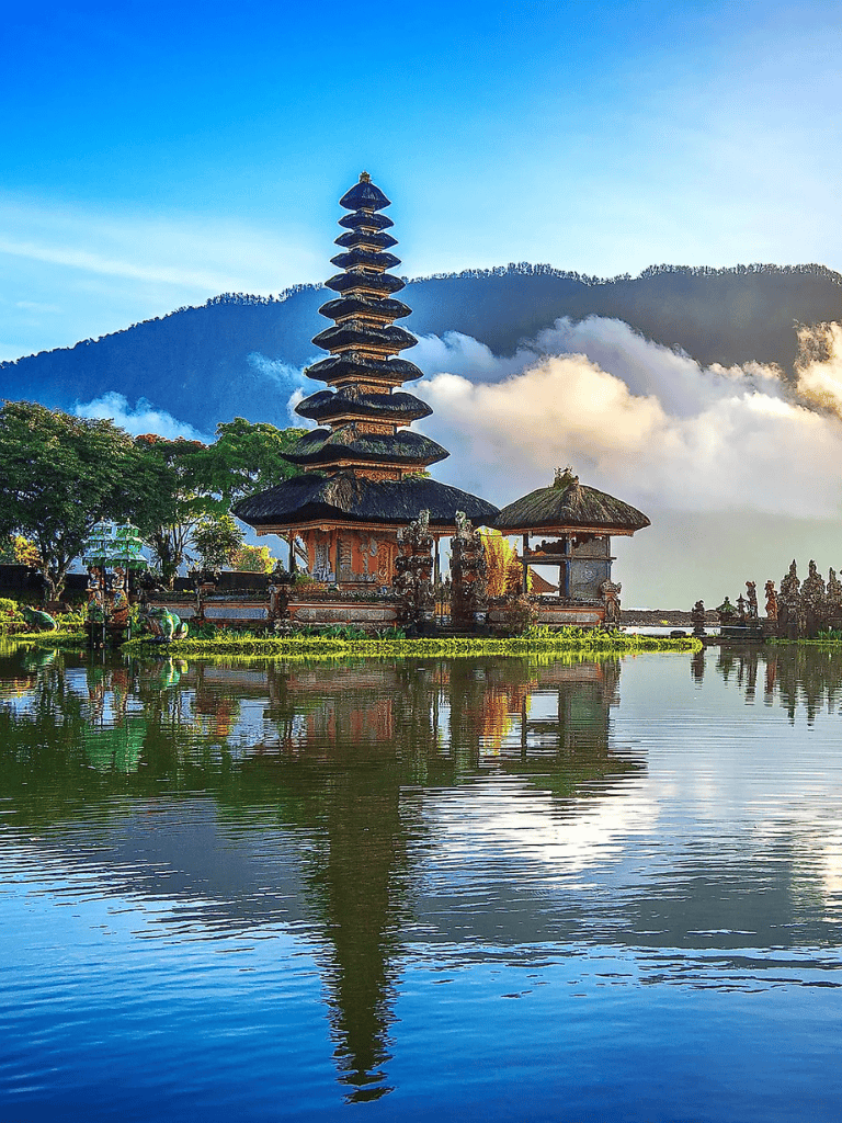 Serene Balinese temple with pagoda reflected in water, lush greenery, and mountain backdrop.