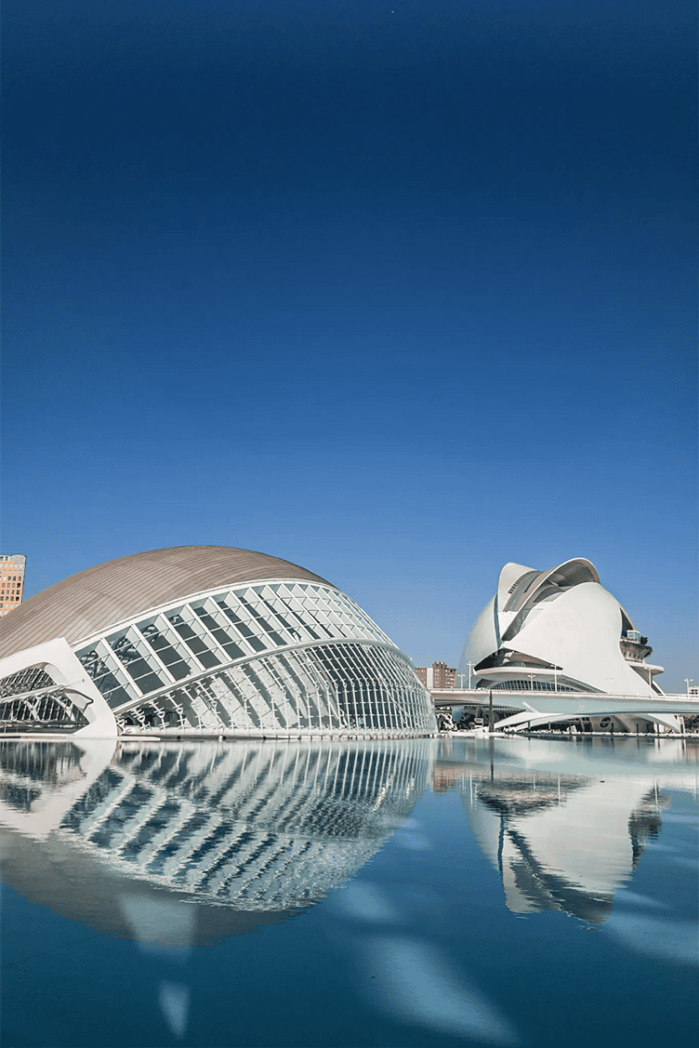 Modern architectural landmarks in Valencia, Spain with reflective water features and clear blue sky.