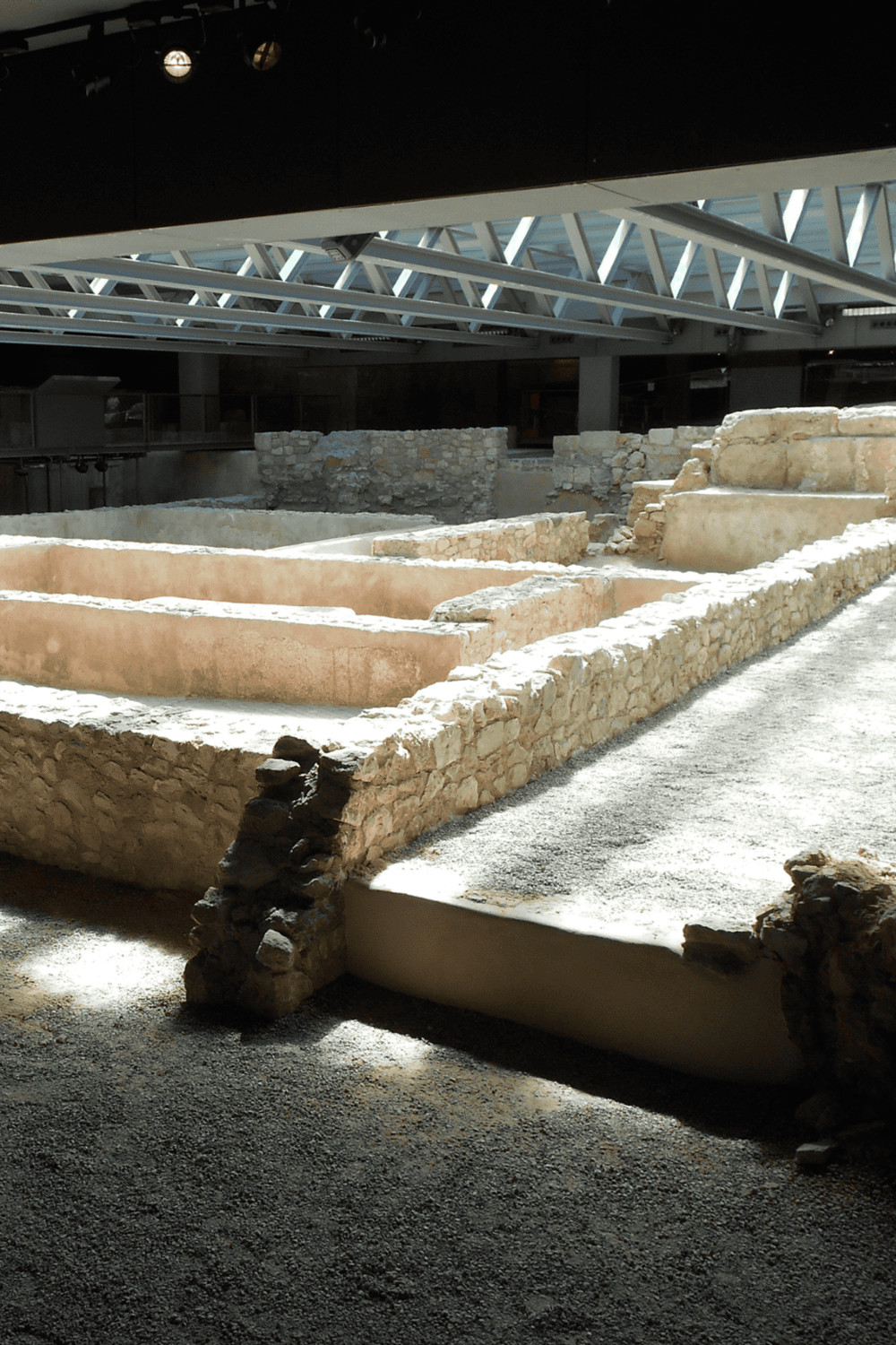 Ancient archaeological ruins displayed inside a modern museum with structural metal beams overhead.